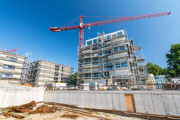 Baustelle mit Baukran und Fundament eines Neubaus und Wohnungen im Hintergrund